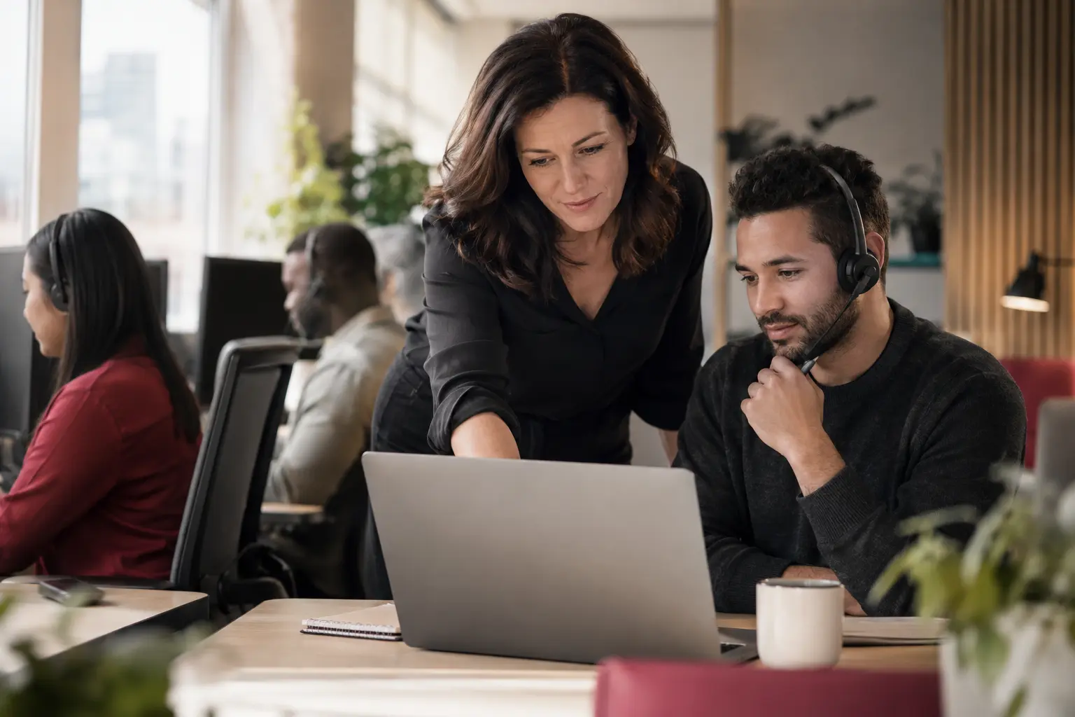 A support supervisor reviewing a conversation summary with a colleague at a laptop in a calm service center.