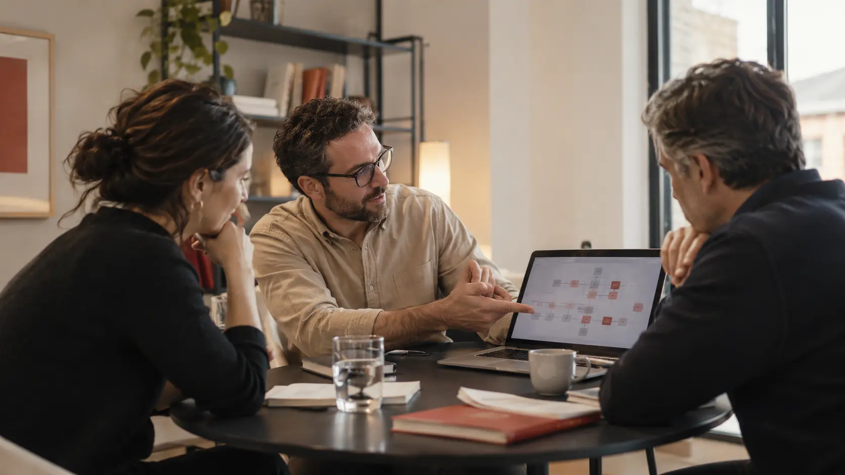 A consultant explaining a workflow prototype to two business staff at a small meeting table, people actively discussing the work rather than posing.